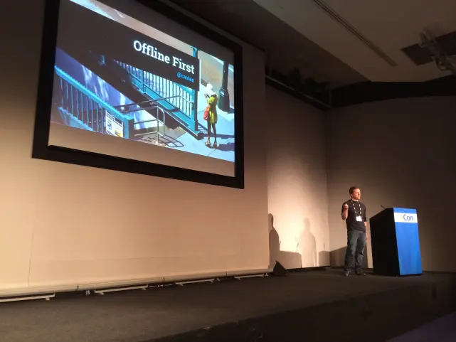 Caolan on stage at QCon London. The slide behind him reads 'Offline First'.